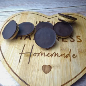 Six keto peanut butter cups arranged on a heart-shaped wooden board