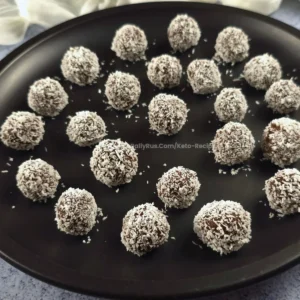 Multiple keto chocolate rum balls on a black plate, rolled in coconut.
