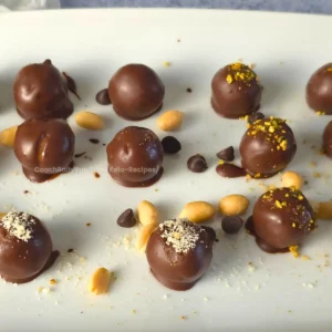 Keto Chocolate Peanut Butter Cottage Cheese Bonbons on a white plate with peanuts and chocolate chips.