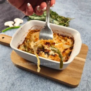 A forkful of cheesy keto green bean casserole with mushrooms and crispy onion topping.