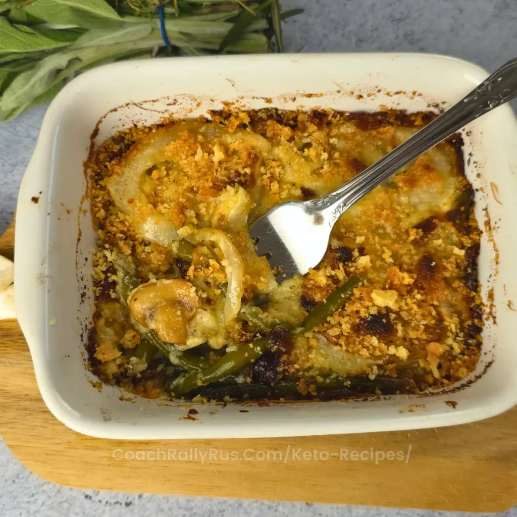 Partially eaten keto green bean casserole in a white baking dish on a wooden serving board.