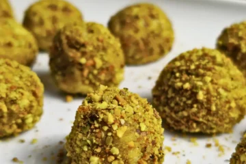 Close-up of keto pistachio cottage cheese bonbons fully coated in crushed pistachios on a white plate.