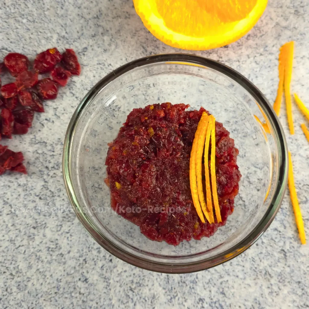 A bowl of vibrant Spiced Keto Cranberry-Orange Relish garnished with orange zest, perfect for low-carb holiday meals.