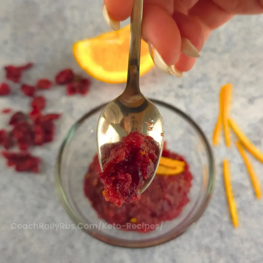 A spoonful of vibrant keto cranberry-orange relish, sugar-free and perfect for holiday meals, held above a serving bowl.