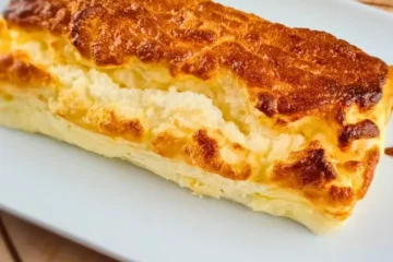 A golden brown, fluffy piece of 2 Ingredient Cottage Cheese Bread served on a white plate, with a pink cloth and three eggs in the background.