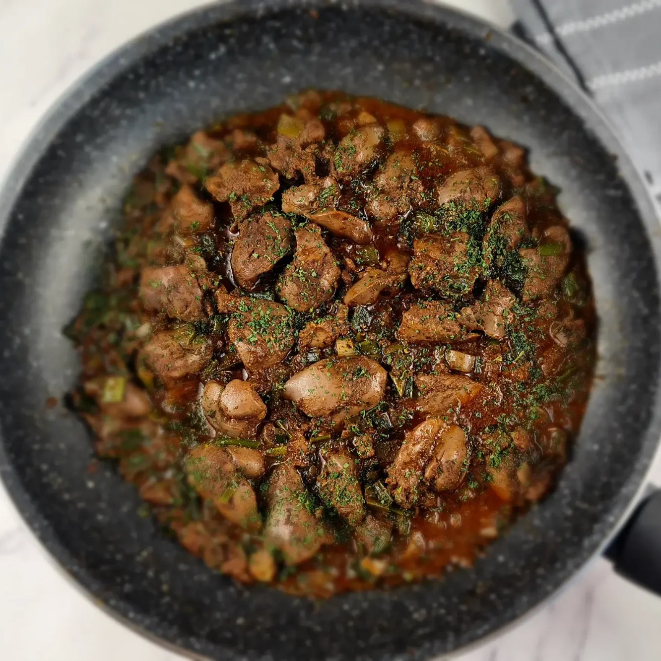 A sizzling pan of keto chicken liver mixed with herbs, cooked to perfection and ready to be served with cauliflower mash.