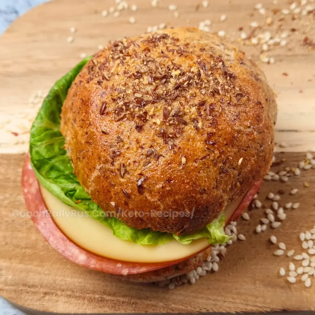 Close-up of a keto flaxseed cottage cheese bread roll sandwich with lettuce, cheese, and salami on a wooden board.