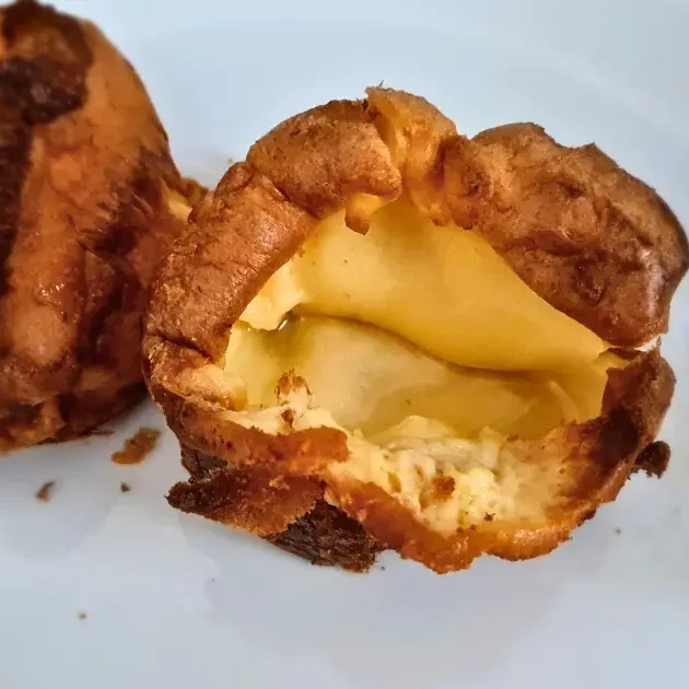 Two keto Yorkshire puddings on a white plate. The puddings are golden brown in color and have a crispy texture. The plate is white and has a red rim.