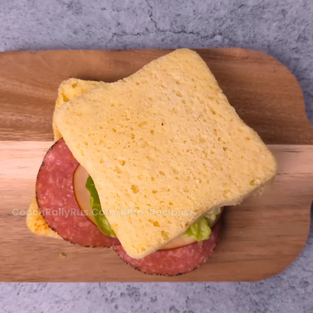 Keto cottage cheese mug bread sandwich with cheese and salami on a wooden board.