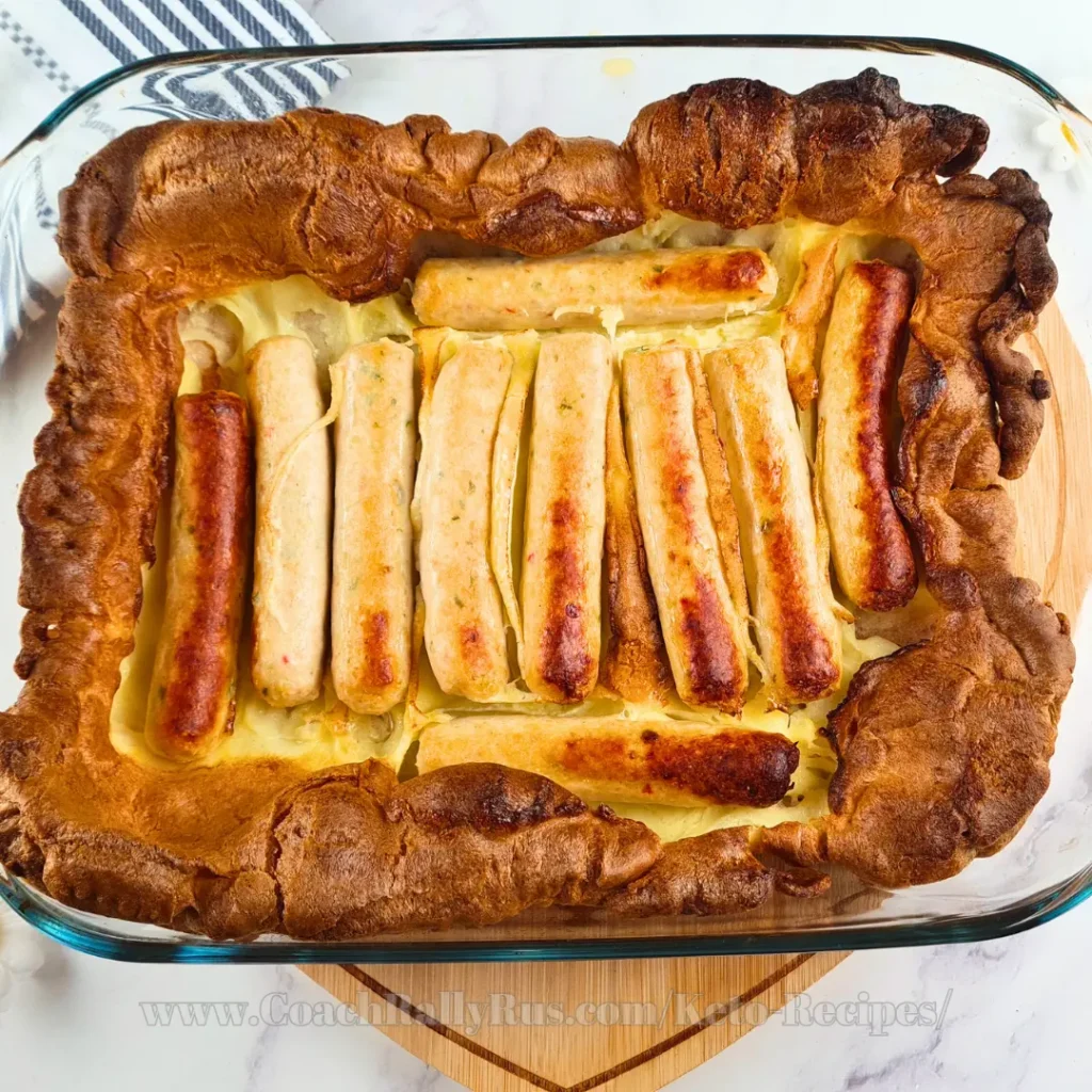 Golden-brown keto toad in the hole with sausages nestled in a fluffy, gluten-free batter baked in a glass baking dish.