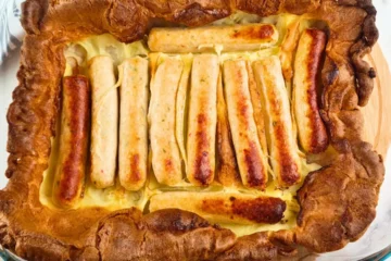 Golden-brown keto toad in the hole with sausages nestled in a fluffy, gluten-free batter baked in a glass baking dish.
