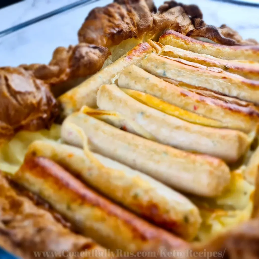 Freshly baked keto toad in the hole with crispy edges and evenly browned sausages arranged in a glass baking dish.