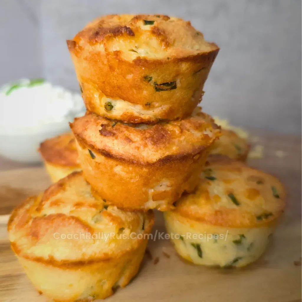 A stack of three golden brown keto cheddar chive biscuits on a wooden board.