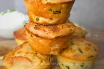 A stack of three golden brown keto cheddar chive biscuits on a wooden board.