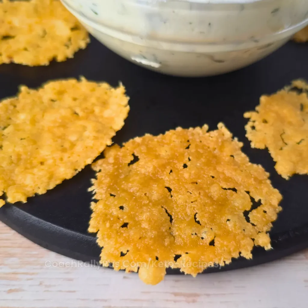 Parmesan cheese chips arranged around a bowl of creamy ranch dip with fresh herbs.