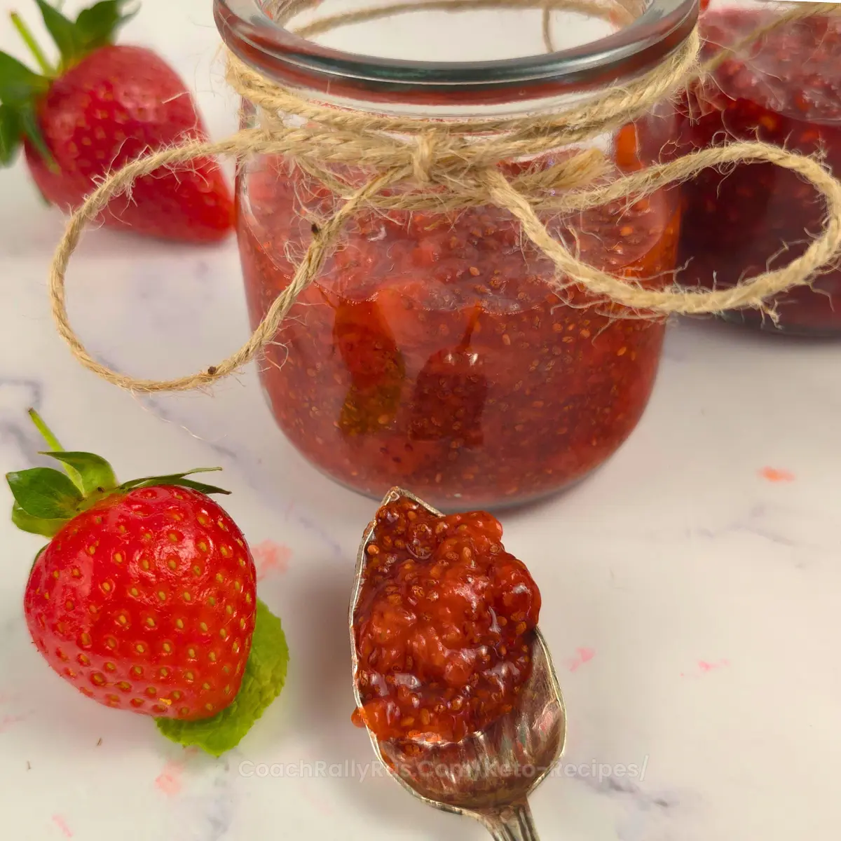 Spoon of thick strawberry chia jam next to jar and fresh strawberries