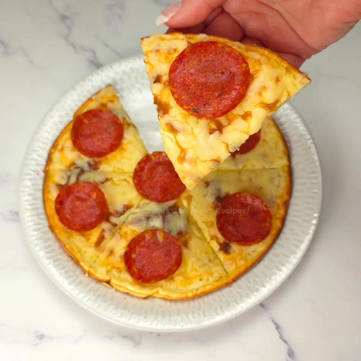 Hand lifting a slice of pepperoni cottage cheese pizza