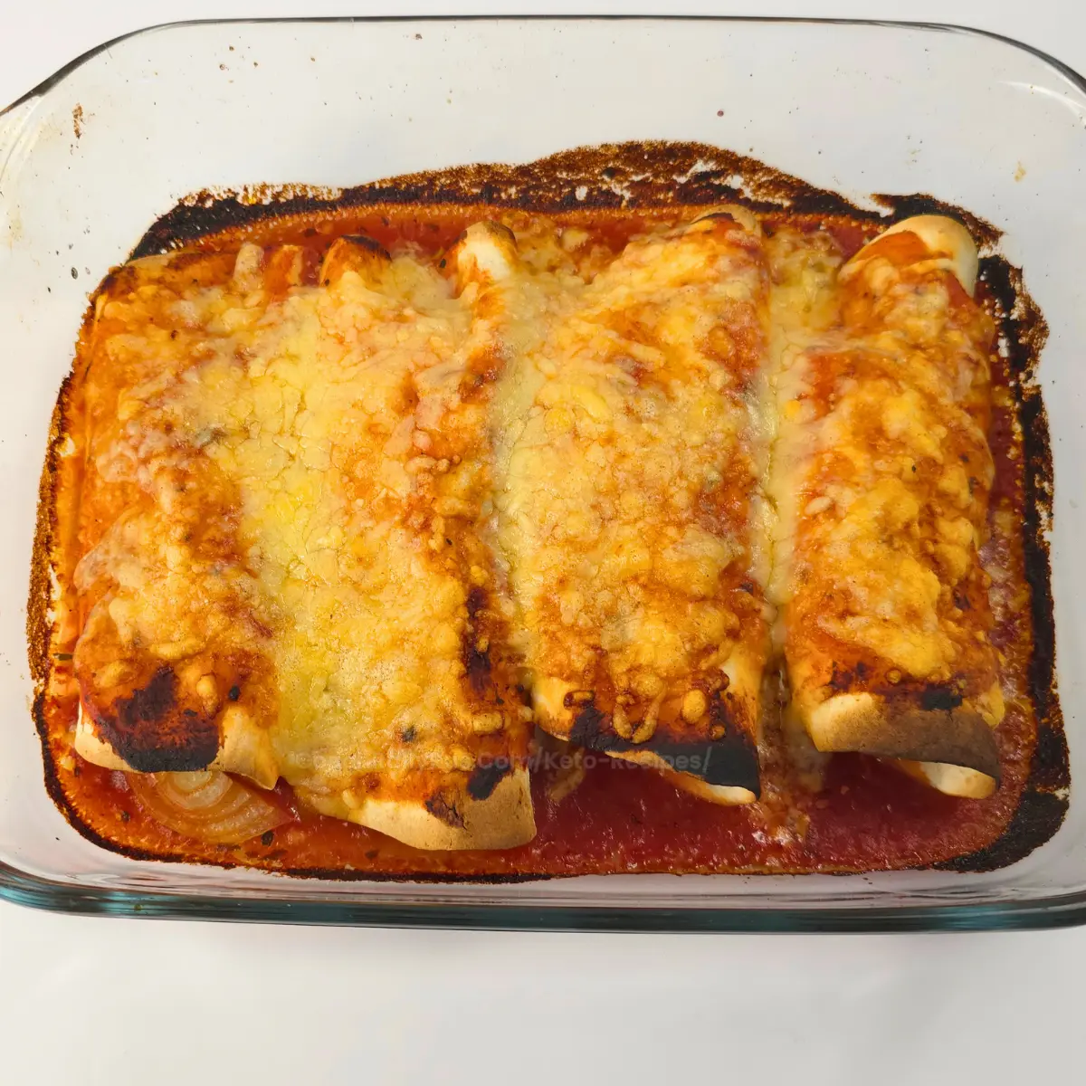 Close-up of keto chicken gyro enchiladas with melted cheese in casserole dish