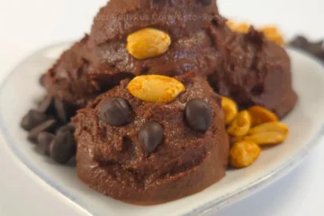 Chocolate peanut butter cookie dough made with cottage cheese, styled in playful scoops on a white dish, garnished with roasted peanuts and chocolate chips