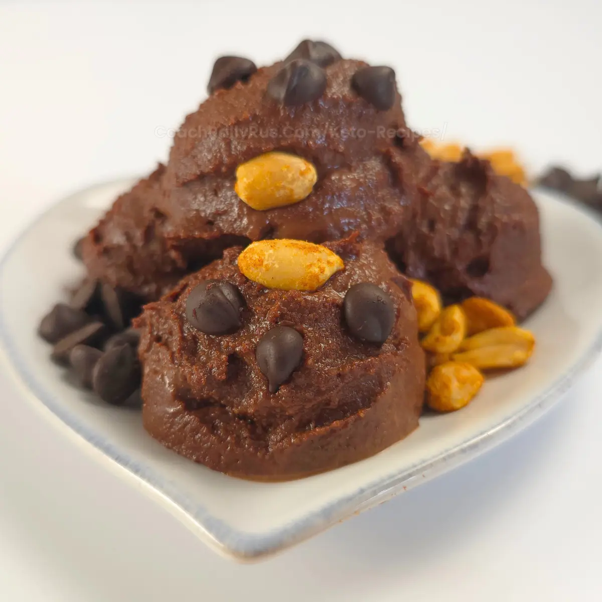 Chocolate peanut butter cookie dough made with cottage cheese, styled in playful scoops on a white dish, garnished with roasted peanuts and chocolate chips