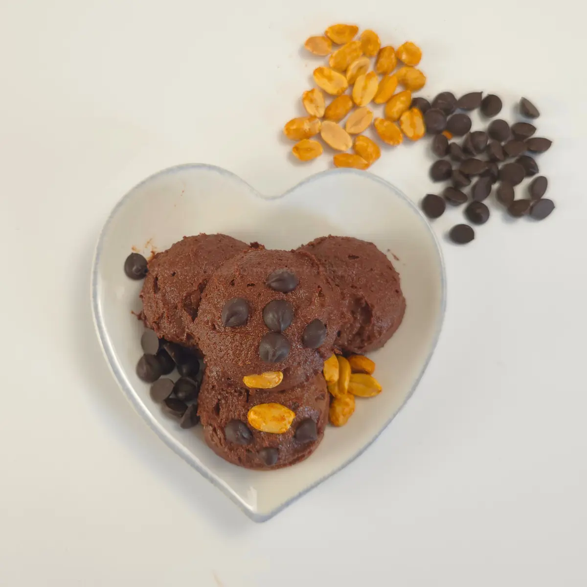 Keto chocolate peanut butter cookie dough topped with peanuts and chocolate chips in heart-shaped bowl