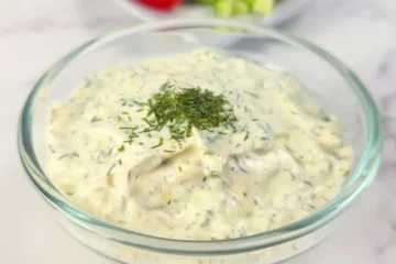 Creamy keto tzatziki sauce with sour cream in a glass bowl with garnish