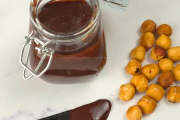 Keto Nutella in glass jar with roasted hazelnuts and chocolate spread on knife