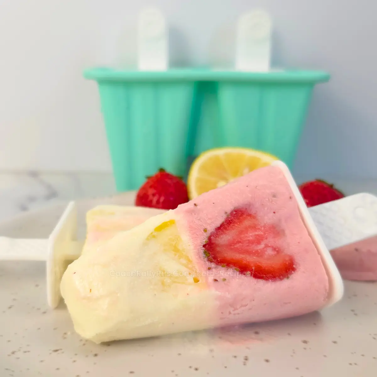 Strawberry lemonade cottage cheese popsicles on marble background with mold and fruit.