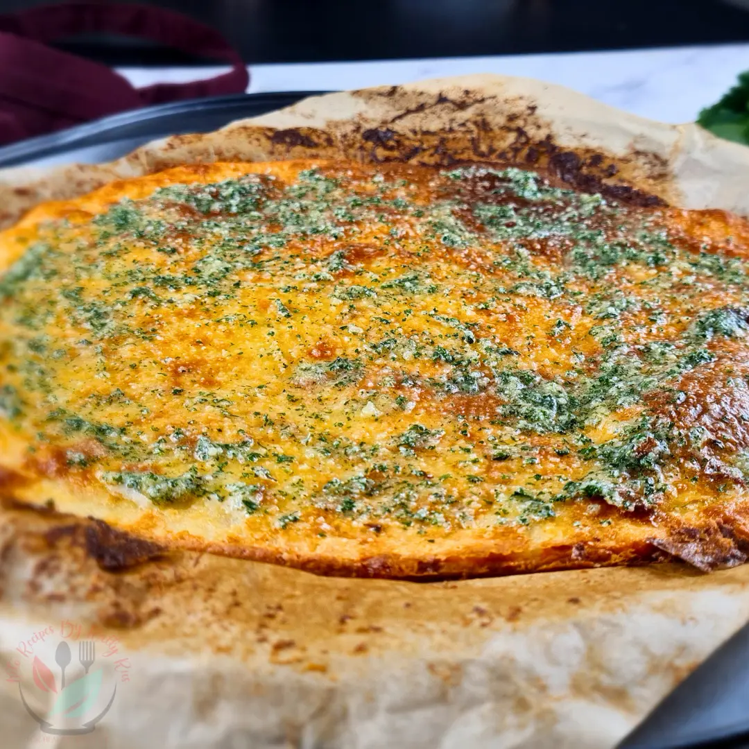 Keto Garlic Bread Recipe with Creme Fraiche Freshly baked keto garlic bread with golden brown edges and parsley butter topping on parchment.