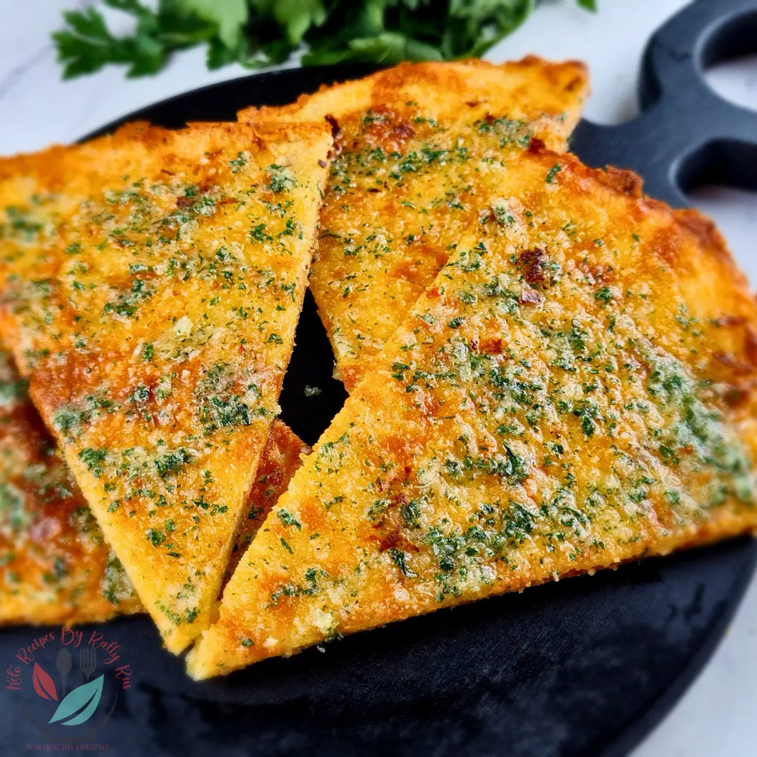 Keto Garlic Bread Recipe with Creme Fraiche Crisp keto garlic bread triangles topped with garlic butter and parsley on a black serving skillet.