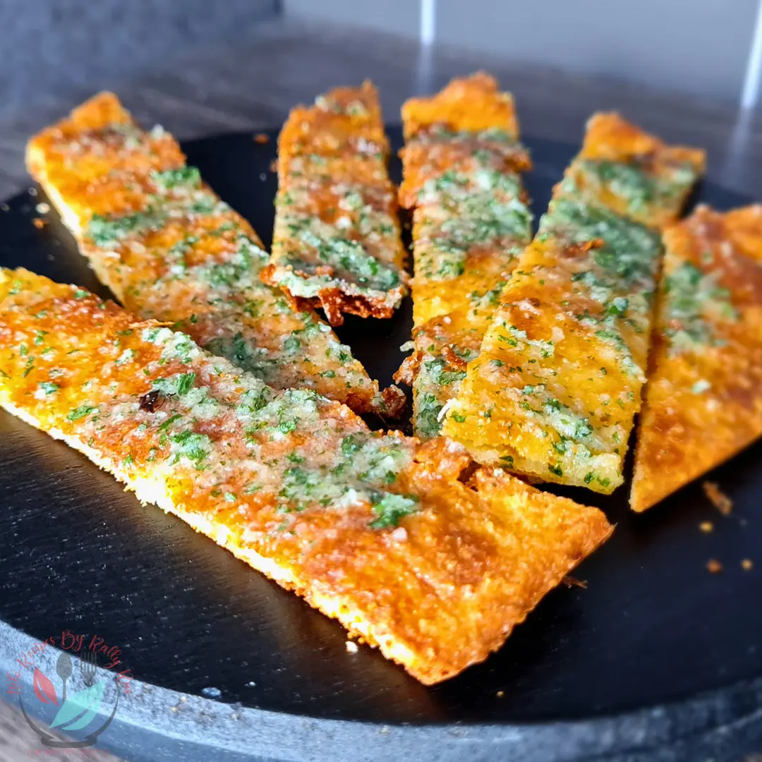 Keto Garlic Bread Recipe with Creme Fraiche Thin keto garlic breadsticks with golden cheese edges and green parsley flakes on a black plate.