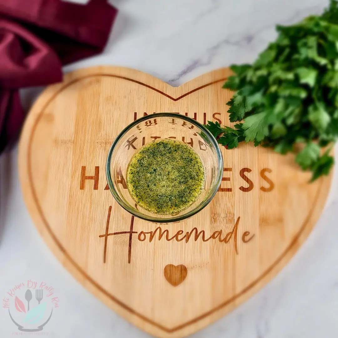 Keto Garlic Butter Homemade garlic butter with parsley and seasoning in a clear glass bowl on a wooden board.