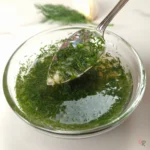 Close-up of a spoonful of fresh dill and garlic vinegar sauce in a glass bowl
